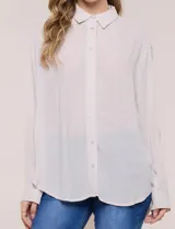 Camisa Magaschoni de silueta holgada y tejido texturizado color blanco, con cuello camisero, cierre frontal de botones, mangas largas con presilla para arremangar y diseño asimétrico con espalda más larga.