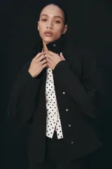 Chaqueta negra de manga larga con cuello subido, bolsillos delanteros y cierre frontal con botones ocultos bajo solapa.