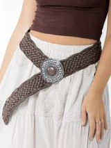 Cinto marrón trenzado con hebilla circular plateada con piedra marrón al centro.