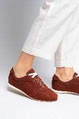 Zapatilla de gamuza color bordó con cordones bicolores, interior de cuero vacuno y suela de caucho blanca y beige.