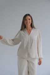 Blusa de color beige con cuello mao, cierre frontal con botones y mangas largas abullonadas. Presenta delicados bordados florales en la parte superior delantera.