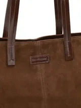 Cartera tipo tote bag de gamuza color marrón, con asas largas de cuero liso y costuras visibles en el centro.