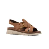 Sandalia plana Korium modelo Adamaris de color beige, confeccionada en gamuza con tiras cruzadas en el empeine, tira ajustable con hebilla metálica dorada y suela dentada en tonos beige y marrón.