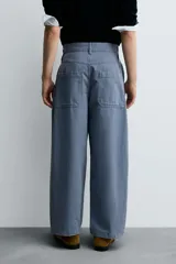 Pantalón de hombre color azul grisáceo, estilo balloon fit, confeccionado en mezcla de algodón y lino. Presenta pliegues en el delantero, cierre frontal con botón y cremallera, bolsillos laterales y bolsillos traseros de plastrón.