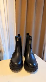 Botas de caña media con cierre frontal metálico, confeccionadas en cuero liso con suela gruesa de goma y plataforma.