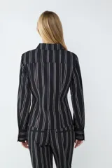 Camisa de manga larga confeccionada en popelina de algodón, con diseño de rayas verticales en tonos oscuros. Presenta cuello clásico, cierre frontal con botones metálicos y dos bolsillos frontales con solapa.