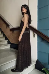 Vestido midi de encaje color marrón oscuro, con cuello halter ajustable con lazadas, detalle de cintura con aplicación de brillos y espalda descubierta. El bajo tiene un acabado en línea evasé.