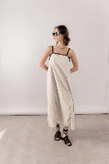 Vestido largo de lino y viscosa color beige, con escote recto, breteles finos negros y detalles de vivos negros en contraste. Presenta un calce amplio y relajado.