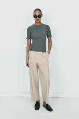 Pantalón de tiro alto con corte recto, bolsillos delanteros y detalle de pinzas con botones en la cintura. Cuenta con cierre frontal de cremallera y gancho metálico.