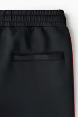Pantalón jogger negro de corte relajado, con cordón ajustable en la cintura, franjas laterales rojas y estampado con la palabra "Honda" en la pierna izquierda.