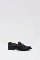 Mocasín de cuero negro con detalle de hebilla metálica plateada en el empeine y suela plana.