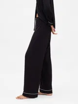 Pijama de dos piezas confeccionado en modal negro, compuesto por una camisa de manga larga con cuello solapa, cierre frontal de botones y vivos en contraste blanco, y un pantalón de corte recto con cintura elástica ajustable mediante cordón y vivos en el ruedo.