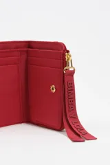 Billetera compacta de estructura blanda en color turquesa, con cierre de cremallera superior y logo metálico dorado en el frente.