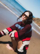 Buzo de tejido grueso con diseño de rayas horizontales en tonos bordó, rojo, blanco, negro y azul claro. Presenta un bordado central en el pecho.