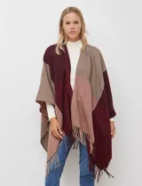 Ruana tejida con diseño colorblock en tonos de gris y beige, con flecos en el borde inferior.