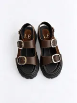 Sandalias de cuero charolado bordó con punta redonda, suela flatform chunky negra con ranuras, y dos tiras frontales con grandes hebillas metálicas plateadas y una tira trasera ajustable.
