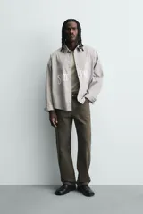 Camisa de corte boxy fit confeccionada en tejido de algodón con diseño de rayas verticales. Presenta cuello solapa, manga larga con puños abotonados y cierre frontal de botones. El frente destaca por bordados y estampados a contraste.