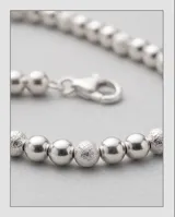 Pulsera de esferas pequeñas de plata 925 con un dije central circular con incrustaciones de cristales.