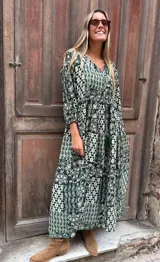 Vestido largo de corte holgado con estampado botánico y geométrico en tonos verdes y blancos. Presenta escote en V con cordones, mangas largas abullonadas con puños elásticos y falda con vuelo.