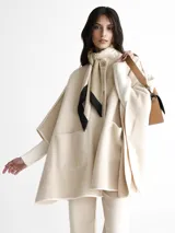 Saco tipo capa color beige con diseño espigado, cuello alto y cierre con un botón.