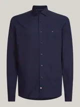 Camisa de manga larga para hombre, color azul marino, de corte slim fit, confeccionada en popelina con tecnología flex que incluye algodón orgánico. Presenta cuello con botones y el logo de Tommy Hilfiger bordado en el pecho.