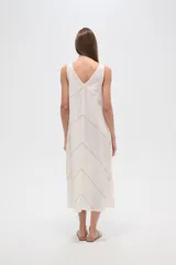 Vestido midi de algodón color crudo, con cuello en V, sin mangas y diseño holgado. Presenta un delicado bordado lineal en forma de zigzag que recorre toda la prenda.