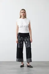 Pantalón de denim negro de corte recto y pierna amplia, con largo al tobillo. Presenta bordados florales en color blanco en la parte frontal superior y en la botamanga.