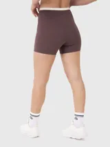 Conjunto deportivo compuesto por un top de entrenamiento color crema con diseño cruzado en la parte inferior y un short biker color marrón con cintura cruzada en contraste.