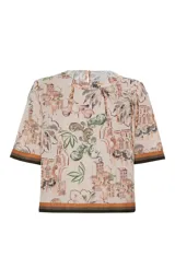 Blusa estampada Le Lis Blanc con diseño de paisaje tropical y arquitectónico, cuello redondo y mangas cortas con ribetes en tonos marrón y negro.