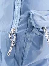 Mochila de diseño clásico en color celeste, confeccionada en material sintético con acabado brillante. Cuenta con un compartimento principal amplio con cierre, un bolsillo frontal externo con cierre y tiradores de cordón trenzado en blanco y negro.