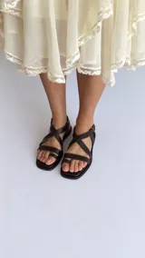 Sandalias de cuero color marrón con diseño de tiras cruzadas en el empeine, sujetador para el dedo y tira ajustable con hebilla en el talón.
