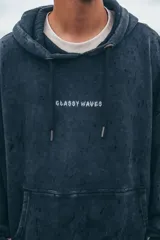 Hoodie de corte oversize en color negro con efecto lavado. Presenta un estampado gráfico en la espalda con la frase 'Glassy Waves' en tipografía estilo llamas, y detalles de llamas estampadas en ambas mangas.