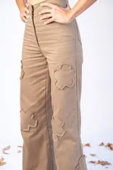Pantalón largo color beige con parches en forma de flor con bordes desflecados.