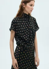 Blusa de viscosa con cuello alto drapeado y mangas cortas. Presenta un diseño recto con estampado de topos en tonos contrastantes sobre fondo negro.