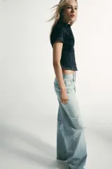 Camisa de denim entallada con cuello solapa, escote en pico y manga corta. Presenta costuras marcadas y cierre frontal con botones.