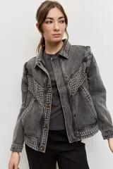 Campera de jean color gris con efecto acid wash, corte clásico y cierre frontal de botones metálicos. Presenta cuello camisero, bolsillos ribeteados y está decorada con apliques de tachas plateadas en el cuello, el canesú frontal, los bordes de la botonera, los bolsillos y el ruedo.
