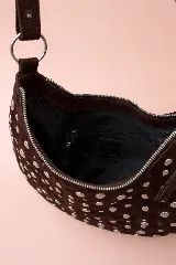 Bolso de mano tipo hobo, confeccionado en gamuza color marrón oscuro, decorado con tachas metálicas circulares en toda su superficie. Cuenta con un asa corta integrada y un diseño curvo distintivo.