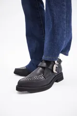 Botín de cuero vacuno color marrón, con punta fina y detalle de tachas metálicas en la parte superior. Presenta una suela de plataforma plana de color negro.