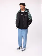 Campera Rusty con capucha, diseño bicolor en negro y verde militar. Presenta cierre frontal, puños elásticos y logo de la marca bordado en el pecho.