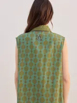 Vestido midi camisero sin mangas, de corte recto y holgado. Cuenta con cuello camisero liso en color naranja y cierre frontal parcial con botones. Presenta un estampado geométrico psicodélico en tonos naranja y beige.