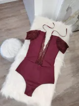 Body de lycra color bordó con mangas cortas de encaje y detalle de encaje vertical en el frente. Presenta un diseño con espalda descubierta y tiras finas para atar en el cuello.