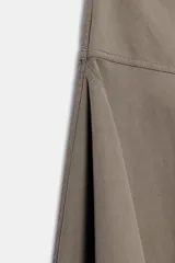 Falda midi de tiro medio color gris, con diseño asimétrico en el bajo, bolsillos frontales y traseros, y cierre frontal con cremallera y botón.