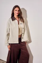 Trench corto de corte oversize con estampado de cuadros finos en tonos beige y verde. Presenta cuello camisero en contraste de color marrón oscuro, cierre frontal con botones y mangas largas con detalle de trabas en los puños.