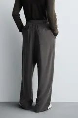Pantalón de corte relajado, color gris oscuro, con cintura elástica ajustable mediante cordón y pliegues frontales. Presenta bolsillos laterales y bolsillos traseros de parche con pespuntes contrastantes.