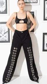 Jean de corte oversize y tiro bajo, color negro, con diseño de argollas metálicas dispuestas verticalmente a lo largo de ambas piernas.