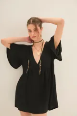 Vestido corto de color negro con escote en V profundo, mangas cortas acampanadas y corte holgado con falda fruncida. Confeccionado en tejido con textura acanalada y acabado brillante.