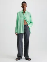 Camisa verde menta de rayón arrugado, corte regular, cuello en punta, manga larga con puños abotonados y espalda dividida con detalle anudado.