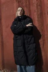 Campera larga acolchonada color marrón, con diseño midi, capucha amplia, cierre frontal con cremallera y broches, y bolsillos delanteros con tapa.