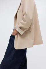 Blazer de sarga color beige, con solapas de pico, frente abierto y bolsillos delanteros ribeteados con solapa.