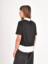 Remera de manga corta con diseño de doble capa, combinando una remera negra lisa con un cuello y ruedo de camisa blanca por debajo.